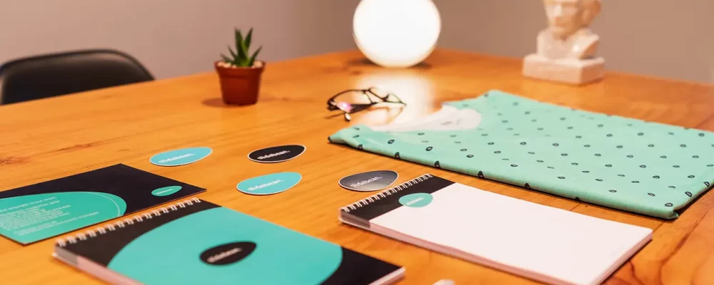 A well-arranged desk with modern stationery, a potted plant, and a decorative lamp, featuring a sleek, turquoise color scheme.